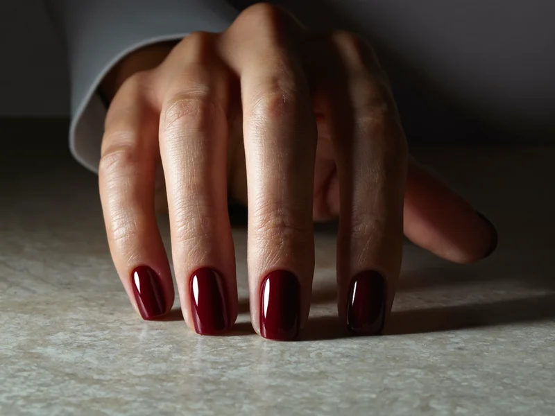 Ongles en vernis gel bordeaux brillant, doigts légèrement écartés sur une surface de pierre claire