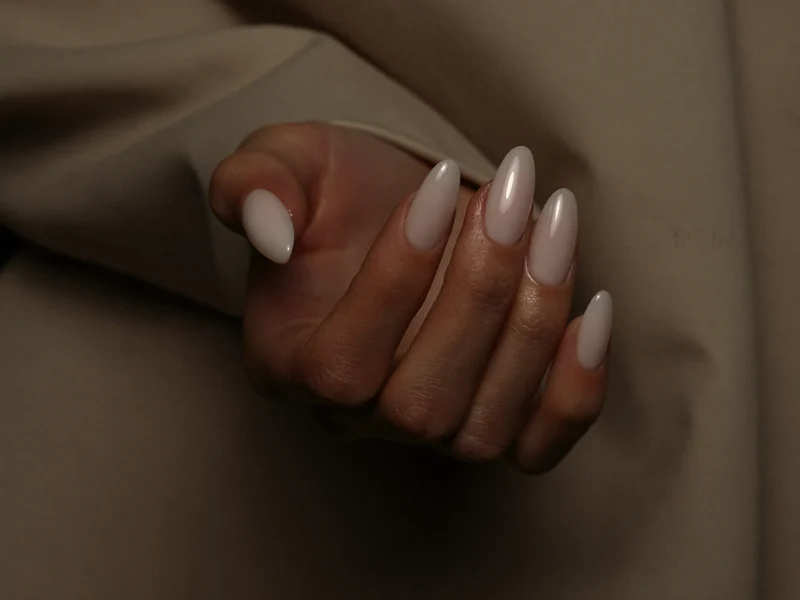 Ongles amande sculptés en rose nude pâle sur un fond de tissu beige