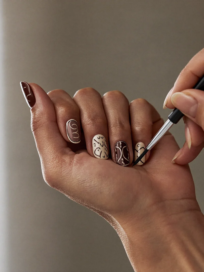 Ongles courts ornés de lignes fines peintes à la main, pinceau visible au bord